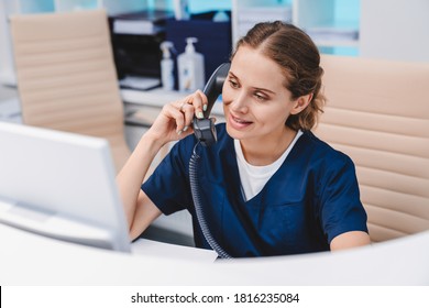 Young female receptionist talking on phone in clinic while sitting and looking on pc monitor - Shutterstock ID 1816235084