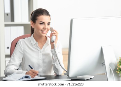 Young female receptionist talking on phone in office - Shutterstock ID 715216228