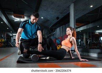 young female relaxing with myofascial release roller with trainer in gym - Shutterstock ID 2062206374