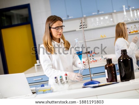 Young female researcher working with blue liquid at separatory funnel in the laboratory