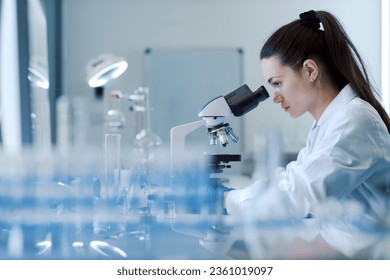 Young female researcher working in the lab, she is examining the samples under a microscope - Powered by Shutterstock