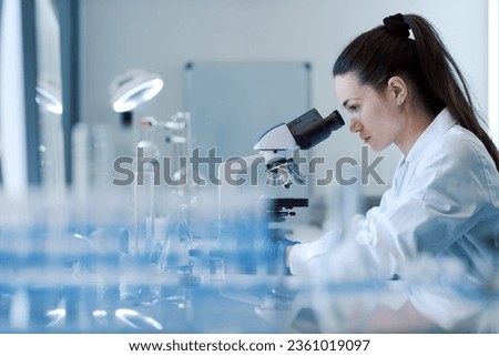 Young female researcher working in the lab, she is examining the samples under a microscope