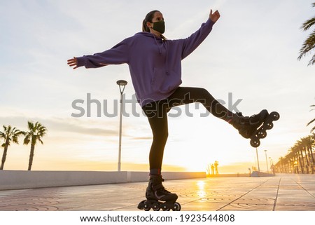 Young female roller skating , posing with open arms and legs , in medical protection mask at sunset.Inline rollerblading sport and healthy creative lifestyle concept during covid-19 pandemic
