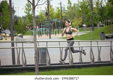 Young female runner, athlete is jogging in tpark in spring sunshine. Beautiful fit caucasian woman training. Concept of fitness, sport, healthy lifestyle, movement, activity and stretching