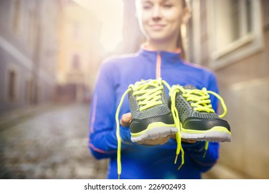 Young Female Runner Carrying Her Running Shoes In Old City Center