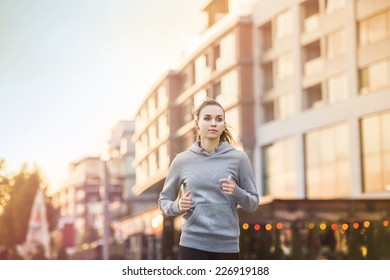 Young female runner in hoody is jogging in the city street - Powered by Shutterstock