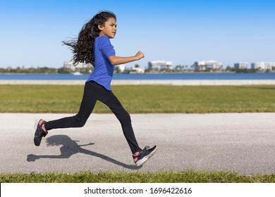 The young female runner looks at a distance as she begins to slow down at the waterfront park. She was captured in midair, running with a defined shadow clearly outlined on the pavement.