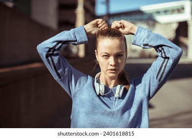 Young female runner tying ponytail before city jog - Powered by Shutterstock