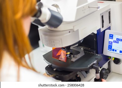  Young female scientist microscoping on hi-tec fluorescent microscope. . Health care professional in hes working environment.
