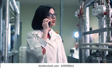 Young Female Scientist Talking Phone Walking In The Factory. Horizontal Indoors Shot.