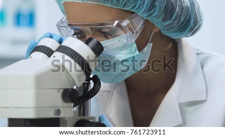 Young female scientist using microscope for microbiological analysis, medicine