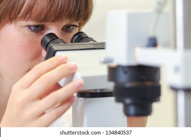 A Young Female Scientist Working In Cancer Research Is Looking Through A Microscope At Cells.