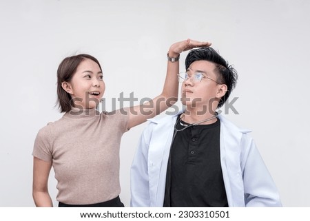 A young female secretary teases the rather average height of her physician friend. Isolated on a red background.