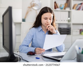 Young female secretary working in the office of a large company is studying the documentation on paper, sitting at ..desktop