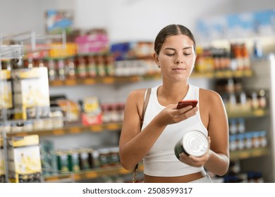 Young female shopper scanning qr code for canned food in supermarket - Powered by Shutterstock