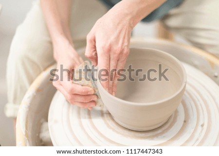 Young female sitting by table and making clay or ceramic mug