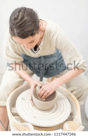 Young female sitting by table and making clay or ceramic mug