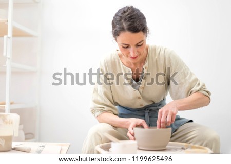 Similar – Young female sitting by table and making clay or ceramic mug