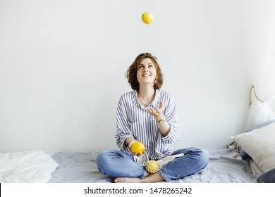 Young Female Sitting On Bed And Juggle Lemons In White Room . Fruit And Healthy Concepts Ideas