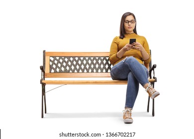 Young female sitting on a bench and typing on a mobile phone isolated on white background