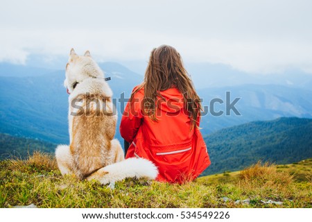 Young female sitting with siberian husky dog in mountains 
