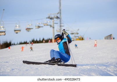 Young Female Skier In Blue Ski Suit Getting Up After The Fall On Mountain Slope Against Ski-lift. Ski Resort. Winter Sports Concept.