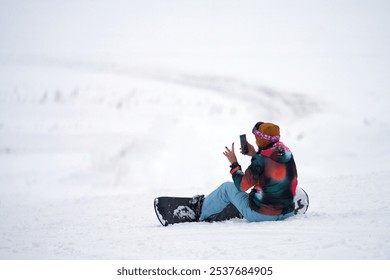 A young female snowboarder sits in the snow on a ski slope and chats on the phone. Copy space.                                - Powered by Shutterstock