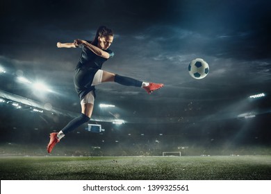 Young female soccer or football player with long hair in sportwear and boots kicking ball for the goal in jump at the stadium. Concept of healthy lifestyle, professional sport, hobby, motion, movement