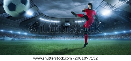 Young female soccer or football player in red kit and boots kicking ball in jump at stadium in flashlights, spotlights in evening. Concept of professional sport, hobby, motion, movement. 3D render.