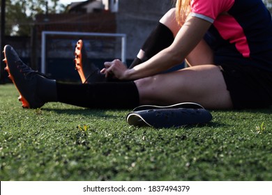 young female soccer player sitting on the grass putting on the boots - Powered by Shutterstock