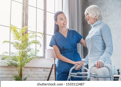 Young female social worker helping senior woman to walk with walker at home - Powered by Shutterstock