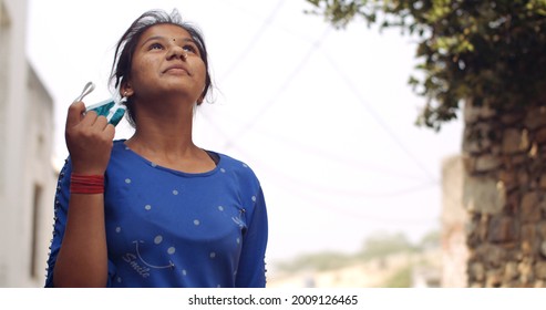 A Young Female South Asian Child Taking Off Her Covid-19 Mask While Looking Up Into The Sky