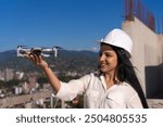 Young female specialist in a hard hat launches a drone at a construction site on a sunny day. Architecture, project management, civil engineering, building inspection.