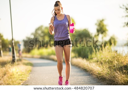 Young female in sportswear walking and resting after  for jogging. She using her smart phone.