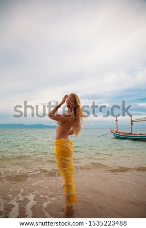 Young female standing at the beach early morning with her feets in the water and waiting for sunrise at the Had Nok beach in Kho Phangan, Thailand. 