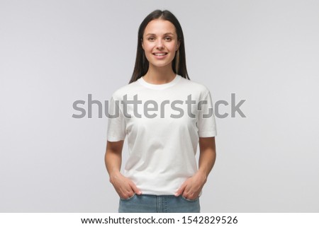 Young female standing in front of camera in white T-shirt and blue jeans, isolated on background