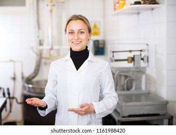 Young Female Standing In Production Workshop In White Overalls