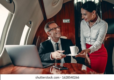 Young Female Stewardess And Senior Business Man Are Flying In Luxury Private Jet.