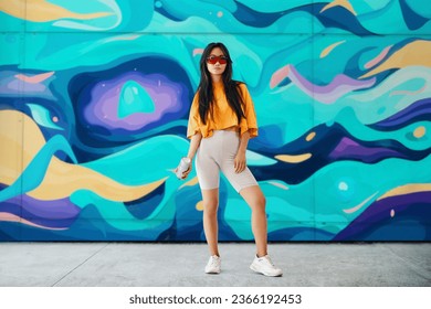 Young female street artist with spray paint can in hand looking to camera over her graffiti wall paintings background. Street art concept. Full length portrait - Powered by Shutterstock