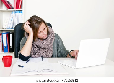 Young female student doing internet research whilst studying her textbooks behind her desk