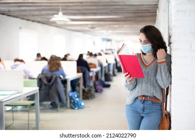 Young female student with face mask reading a book inside a classroom. Presential classes at the university. Space for text. - Shutterstock ID 2124022790