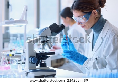 Young female student in the research lab, she is examining a sample in a petri dish and using the microscope