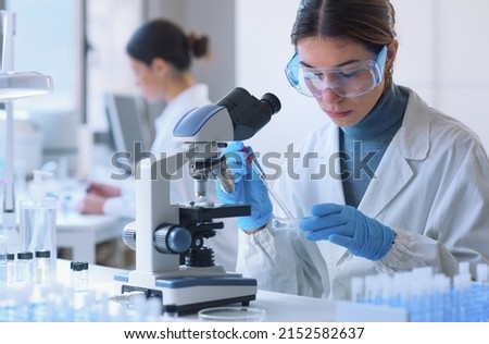 Young female student in the research lab, she is examining a sample in a petri dish and using the microscope