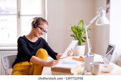 A young female student sitting at the table, using tablet when studying.