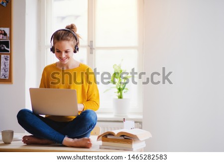 A young female student sitting at the table, using headphones when studying.