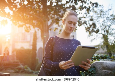 Young Female Student Is Using Touch Pad For Preparing To Exam In University,while Is Standing On Campus. Woman Tourist Is Searching On Digital Tablet Information About History City During Walking Tour