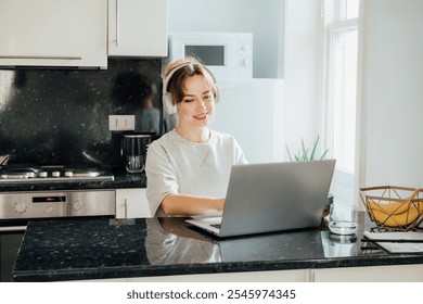 Young female student wear headphone, watch webinar, listen online course communicate by conference video call, e-learn language in app study with teacher lesson look at laptop at home on tiny kitchen. - Powered by Shutterstock