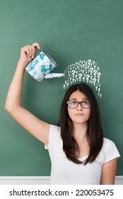 Young female student wearing eyeglasses while pouring interrogation signs over her head from a watering can, creative concept of questions, education and inquiring learning
