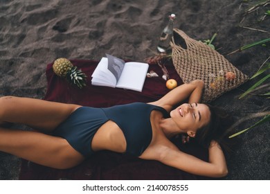 Young female in stylish swimwear enjoying recreation time at coastline beach - nap during leisure for dreaming, happy woman with closed eyes sleeping at seashore - pastime for resting in swimsuit