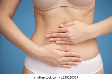 Young Female Suffering From Abdominal Pain. Blue Background, Studio.